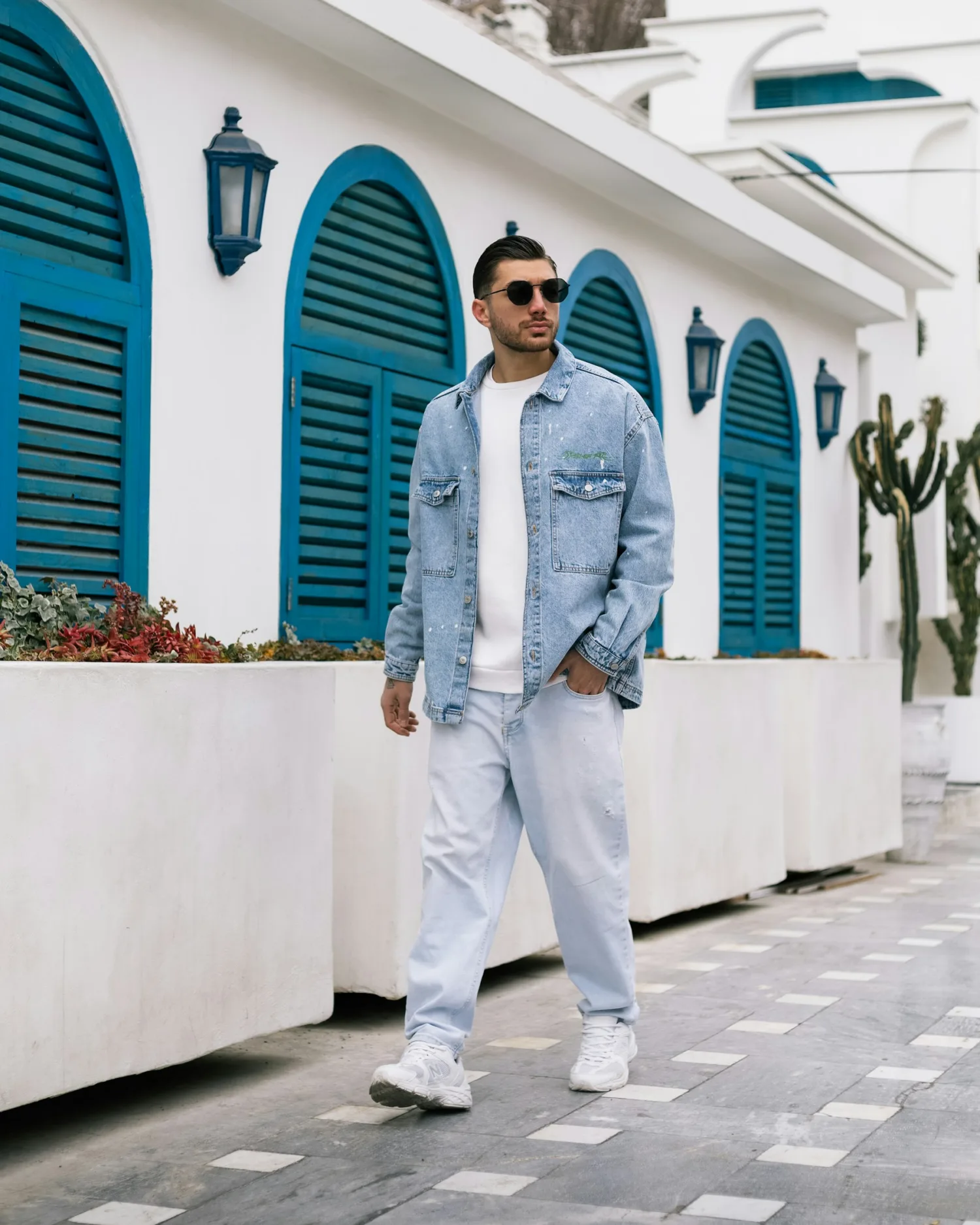 A man wearing a light denim jacket and jeans with a white T-shirt and sneakers