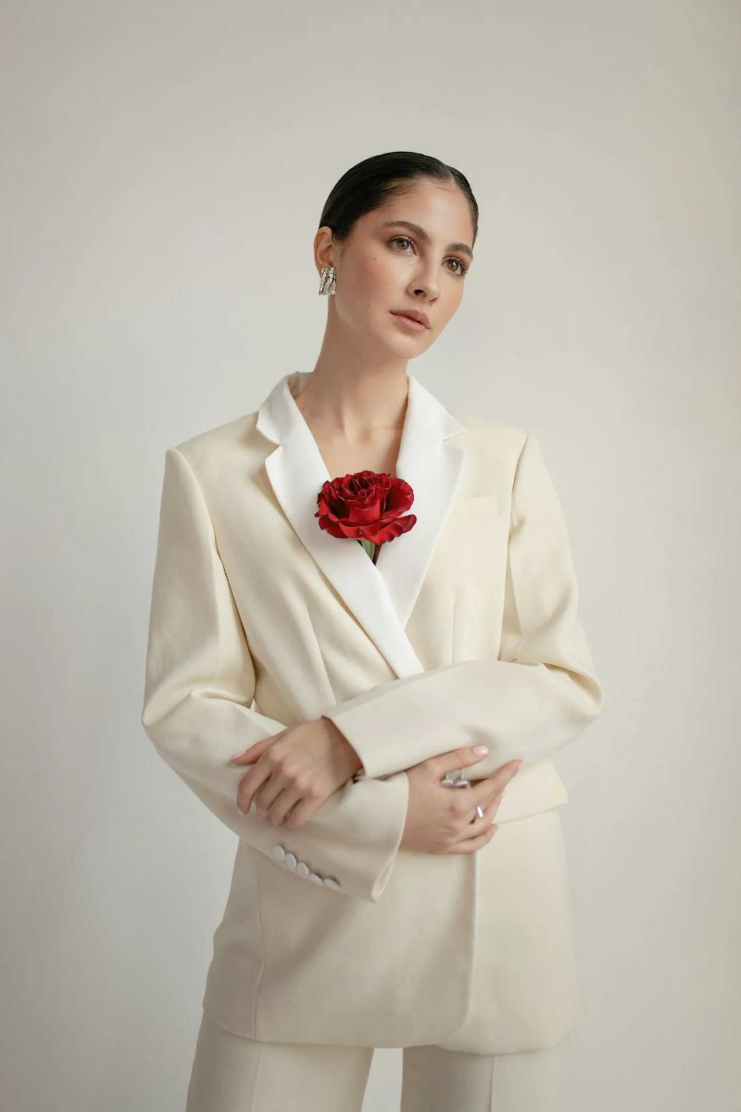 A woman in an ivory tailored suit with a red flower, photographed against a warm neutral background
