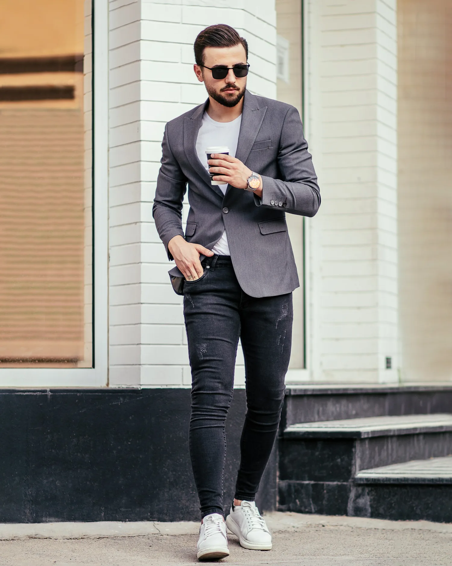 A man styling a gray blazer, white T-shirt, dark jeans, and white sneakers